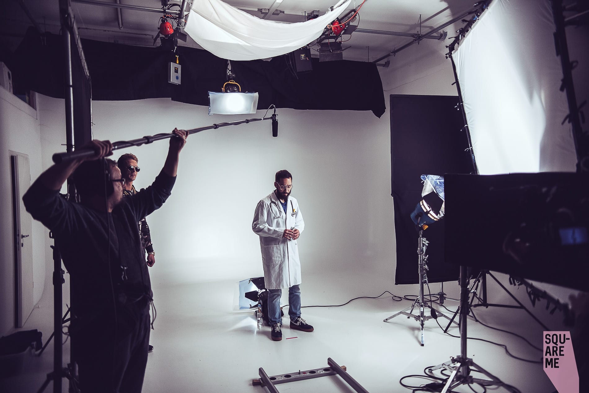 Squareme Proteini.si ad. Luka Štigl as doctor on set in fron of the camera on white background with actor Igor Mikić standing on the side.