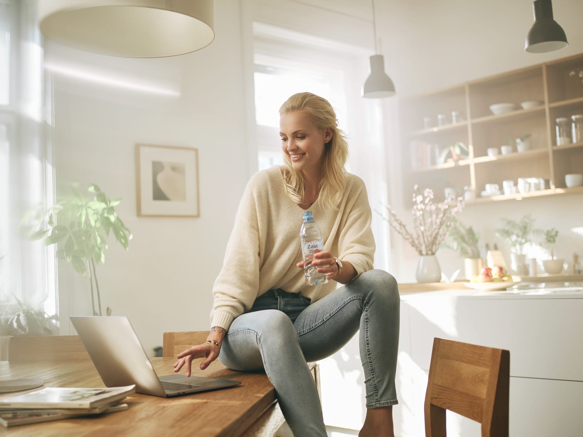 Squareme Zala ad. Tjaša Kokalj, young Slovenian model, sitting on a desk with a bottle of Zala water, working on a laptop computer.