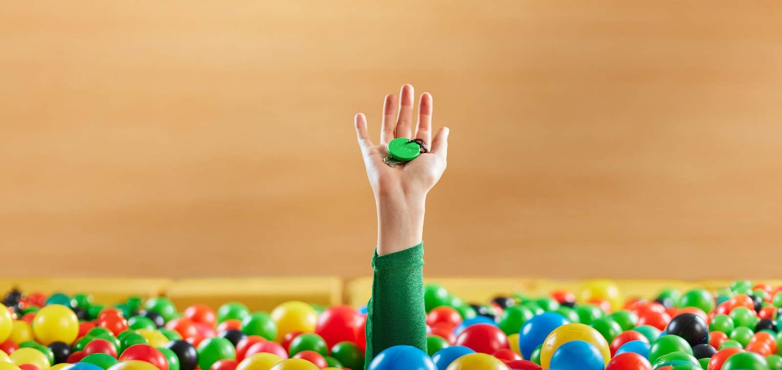 A Chipolo product is held by a hand protruding from a ball pit.